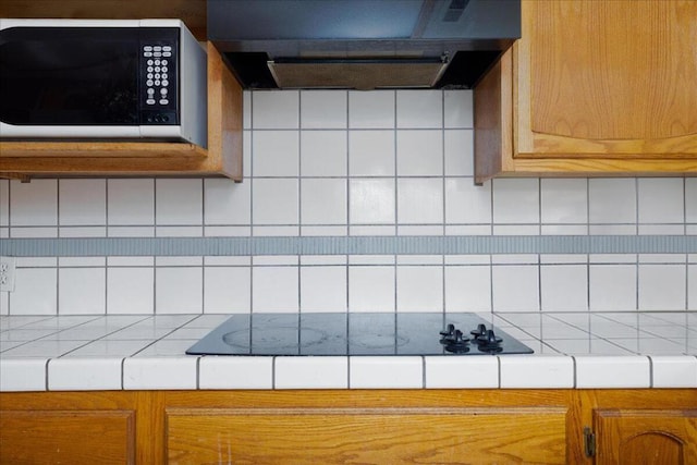 kitchen with tile countertops, wall chimney range hood, backsplash, and black electric cooktop