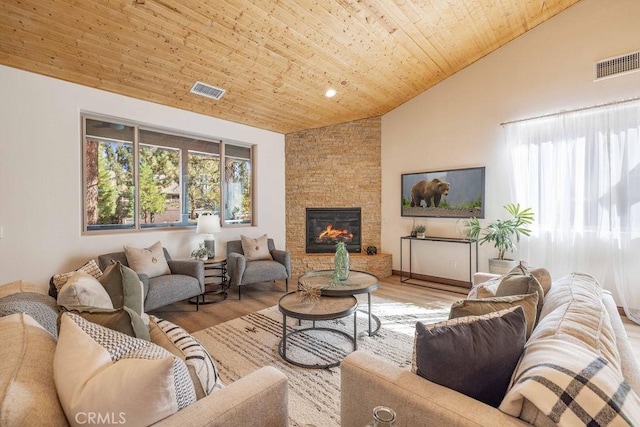 living room featuring high vaulted ceiling, light hardwood / wood-style floors, a stone fireplace, and wooden ceiling