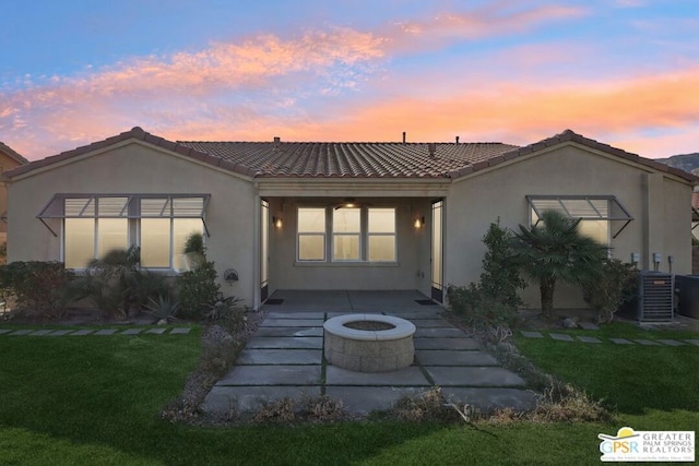 back house at dusk featuring a yard, a patio, central air condition unit, and an outdoor fire pit