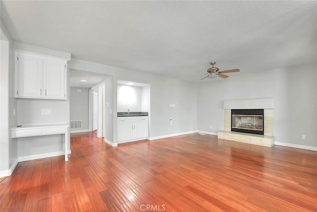 unfurnished living room featuring a textured ceiling, light hardwood / wood-style flooring, ceiling fan, and sink