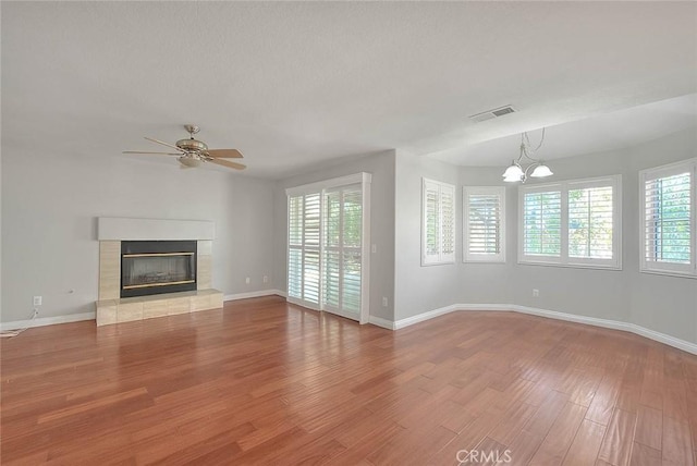 unfurnished living room featuring ceiling fan with notable chandelier, light hardwood / wood-style flooring, and a tiled fireplace