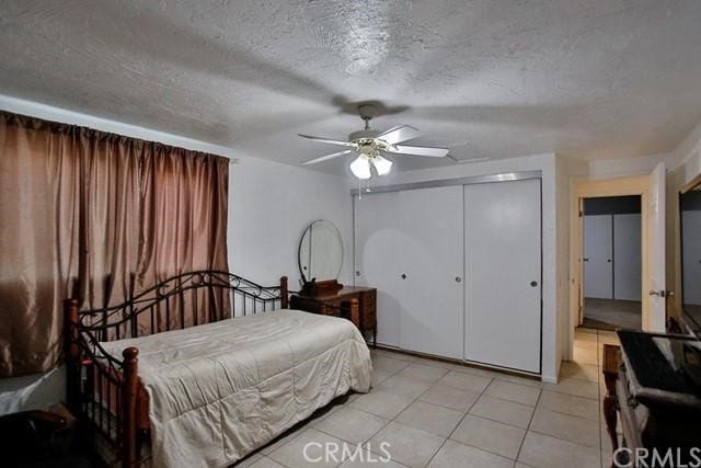 bedroom featuring a closet, ceiling fan, light tile patterned floors, and a textured ceiling