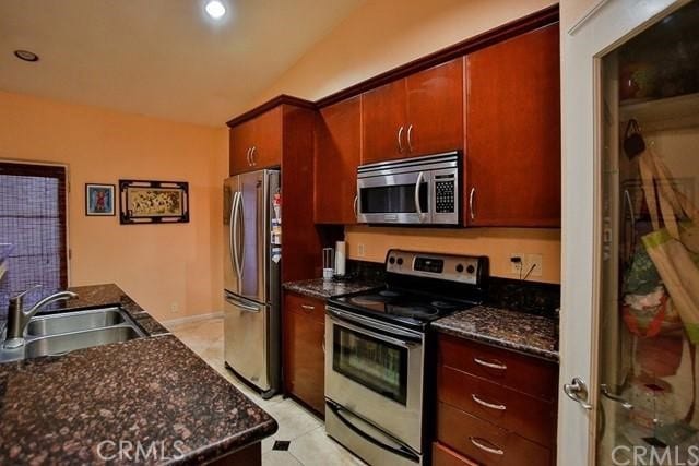 kitchen with dark stone countertops, lofted ceiling, appliances with stainless steel finishes, and sink