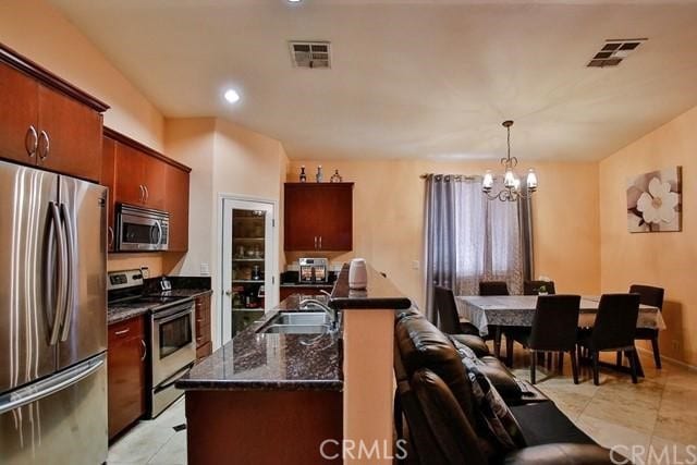 kitchen featuring an island with sink, hanging light fixtures, sink, stainless steel appliances, and a notable chandelier