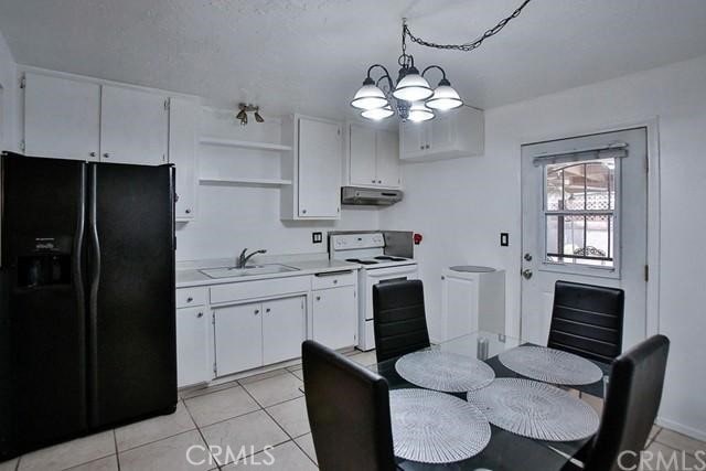 kitchen featuring black fridge, sink, white cabinets, hanging light fixtures, and white electric range