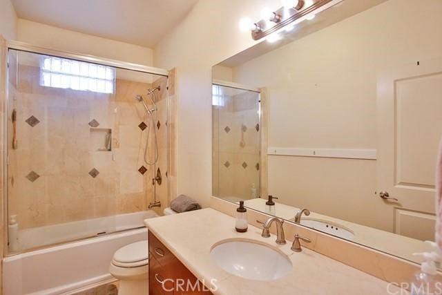 full bathroom with enclosed tub / shower combo, vanity, and toilet