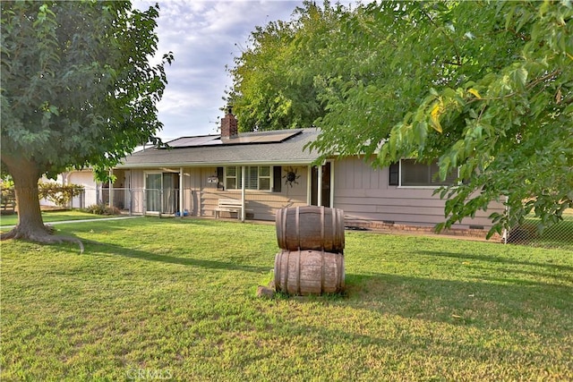 back of house with a chimney, board and batten siding, roof mounted solar panels, and a lawn
