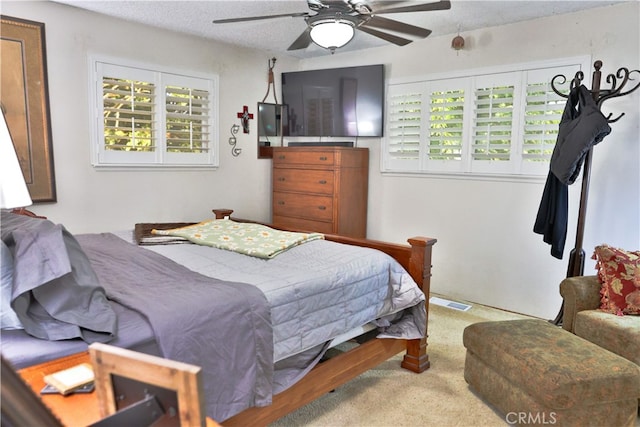 bedroom featuring ceiling fan, a textured ceiling, multiple windows, and light colored carpet