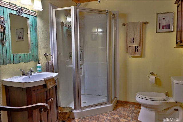 full bathroom featuring a stall shower, toilet, stone finish floor, and vanity