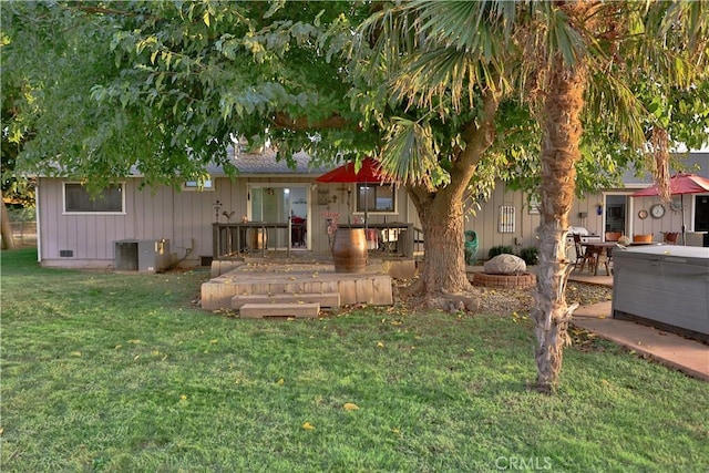 back of property with a lawn, board and batten siding, crawl space, and a hot tub