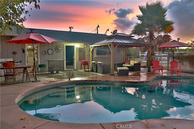 pool at dusk with a gazebo, a patio area, and an outdoor hangout area