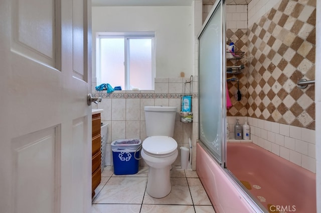 full bathroom with tile walls, vanity, tile patterned flooring, bath / shower combo with glass door, and toilet