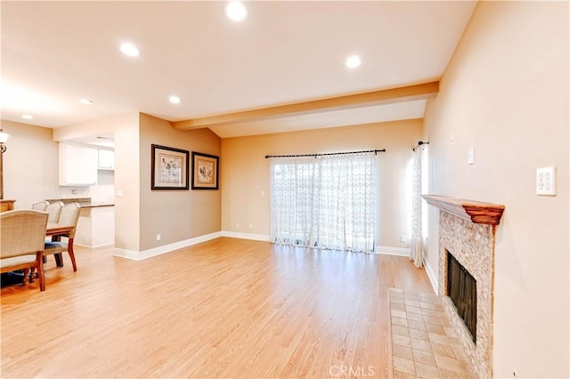 living room with lofted ceiling with beams, a stone fireplace, and light wood-type flooring