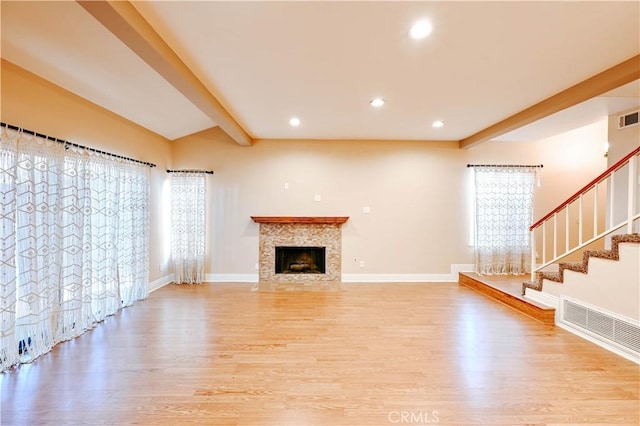 unfurnished living room with beamed ceiling, a premium fireplace, and light hardwood / wood-style floors