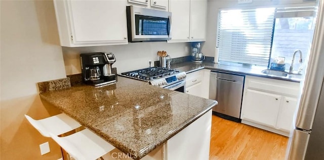 kitchen featuring white cabinetry, sink, dark stone countertops, stainless steel appliances, and light wood-type flooring