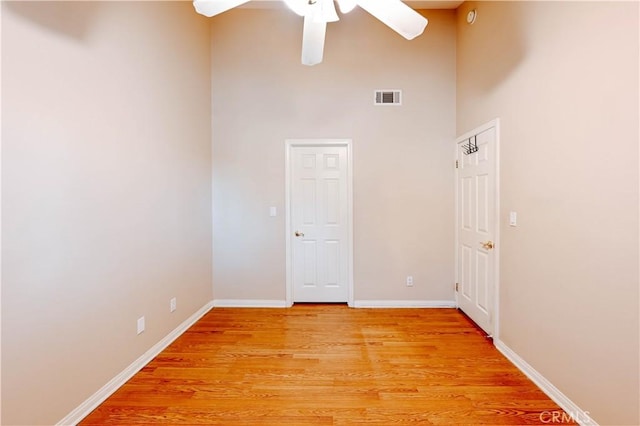 unfurnished room with ceiling fan, a towering ceiling, and light hardwood / wood-style floors