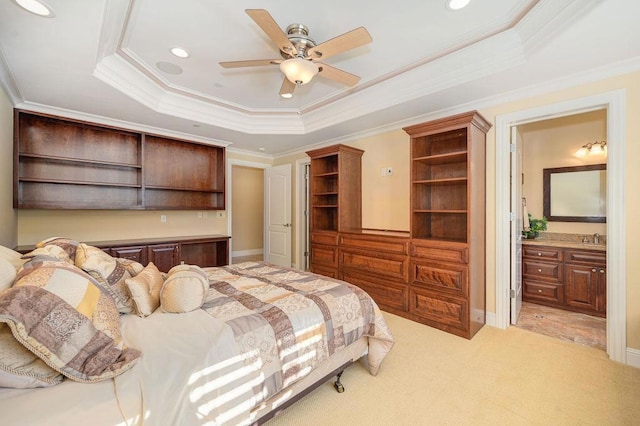 carpeted bedroom with a tray ceiling, ensuite bath, ornamental molding, and ceiling fan