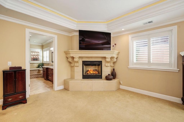 carpeted living room featuring a tiled fireplace, crown molding, a raised ceiling, and a wealth of natural light