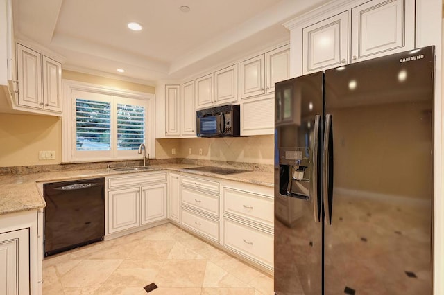 kitchen with a raised ceiling, sink, light stone counters, and black appliances