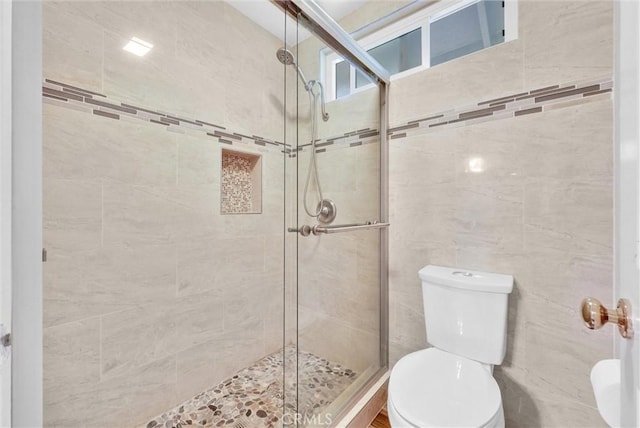 bathroom with toilet, a shower with door, and tile walls