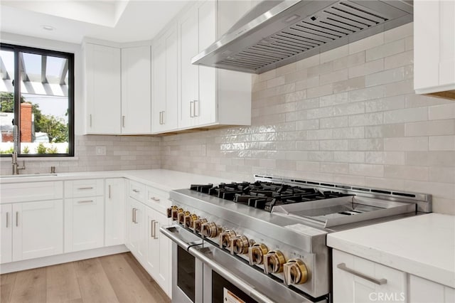 kitchen featuring tasteful backsplash, wall chimney range hood, double oven range, white cabinets, and light hardwood / wood-style floors