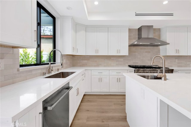 kitchen featuring dishwasher, white cabinets, wall chimney range hood, sink, and light wood-type flooring