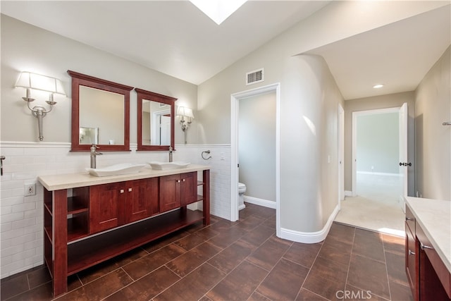 bathroom with tile walls, vaulted ceiling, toilet, and vanity