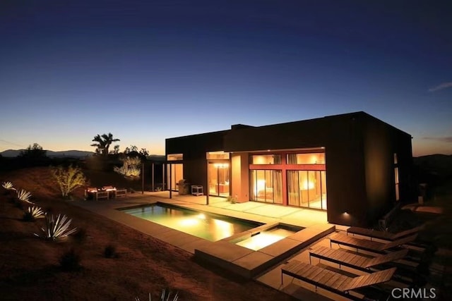 back house at dusk featuring a pool with hot tub and a patio area