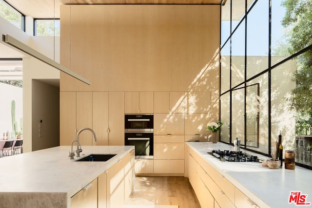 kitchen with an island with sink, stainless steel gas cooktop, light wood-type flooring, black double oven, and sink