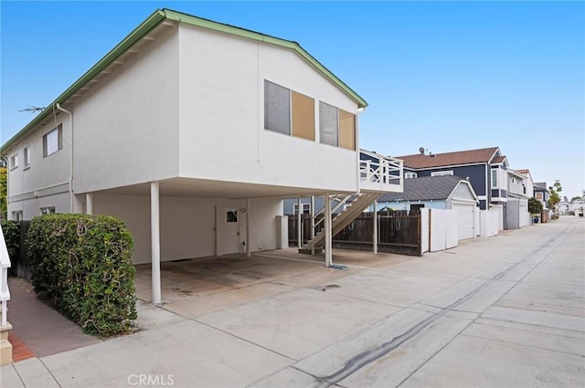 rear view of property featuring stucco siding, a residential view, stairs, and fence