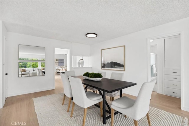 dining space featuring baseboards, a textured ceiling, and light wood-type flooring