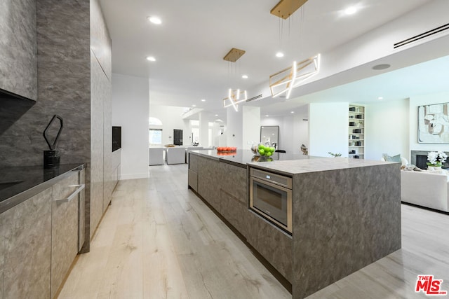 kitchen featuring light wood-type flooring, hanging light fixtures, a spacious island, and stainless steel oven