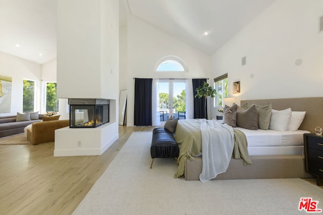 bedroom featuring light hardwood / wood-style floors, a multi sided fireplace, and high vaulted ceiling