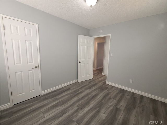 unfurnished bedroom with a textured ceiling, dark hardwood / wood-style floors, and a closet