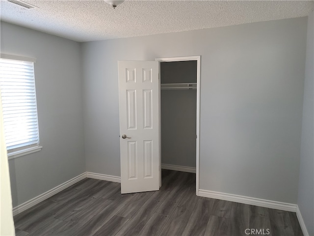 unfurnished bedroom featuring a textured ceiling, dark hardwood / wood-style flooring, and a closet