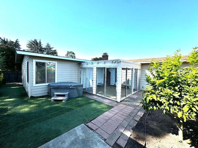 rear view of house featuring a hot tub, a patio, and a lawn