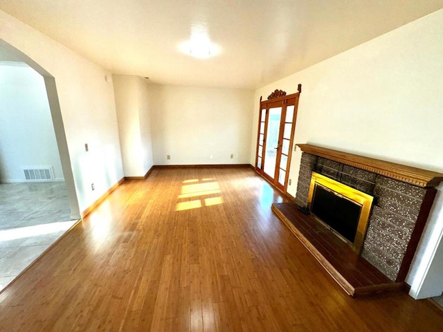 unfurnished living room featuring a tile fireplace, wood-type flooring, and french doors