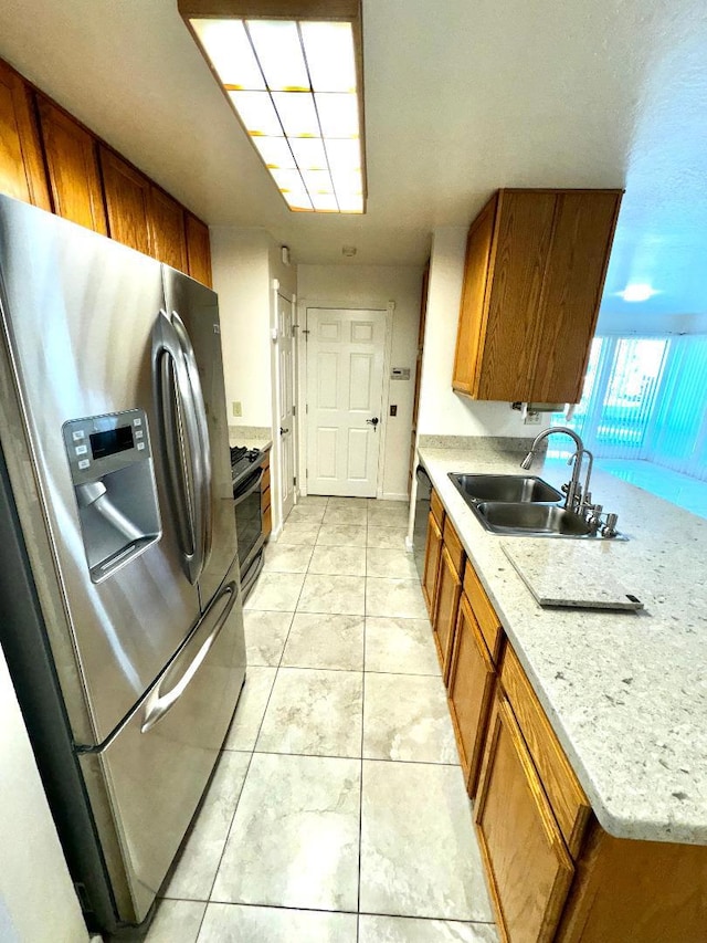 kitchen with sink, stainless steel refrigerator with ice dispenser, light stone counters, light tile patterned flooring, and range with gas cooktop