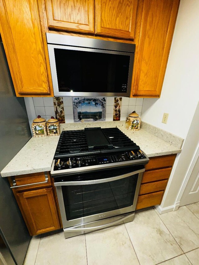 kitchen with light tile patterned flooring, appliances with stainless steel finishes, light stone countertops, and backsplash