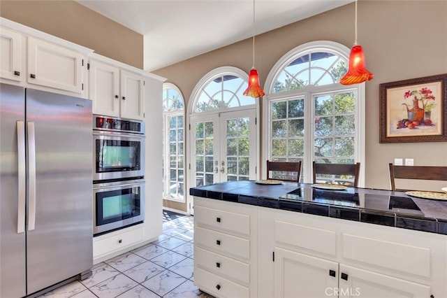 kitchen featuring french doors, stainless steel appliances, pendant lighting, white cabinetry, and tile counters