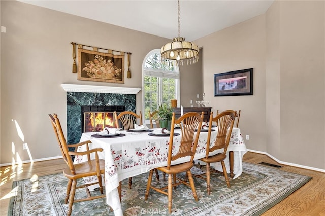 dining area featuring lofted ceiling, a chandelier, hardwood / wood-style floors, and a premium fireplace