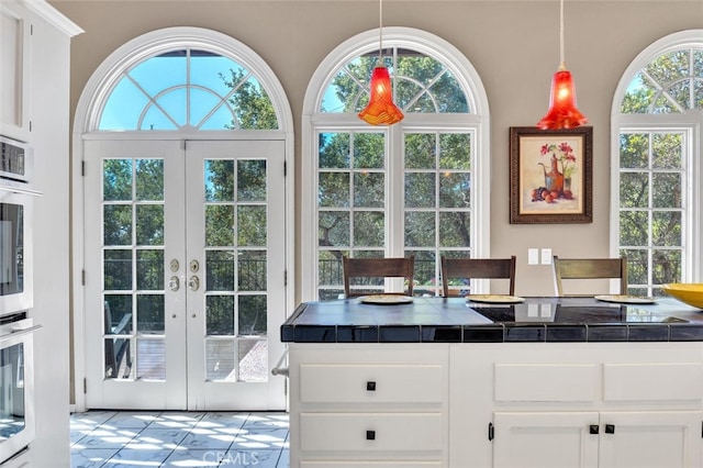 kitchen with pendant lighting, french doors, white cabinetry, tile countertops, and tile patterned flooring