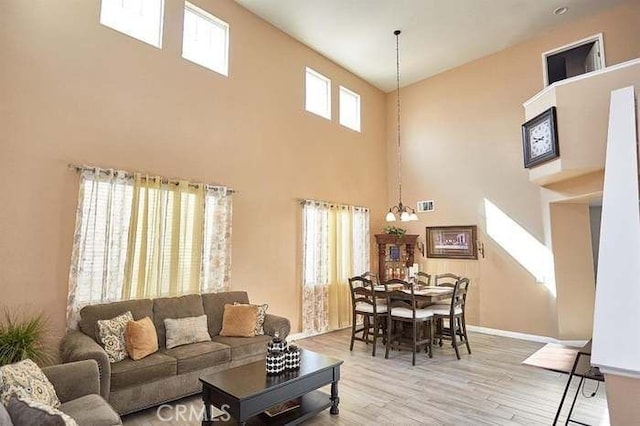 living room featuring a towering ceiling, an inviting chandelier, light hardwood / wood-style flooring, and plenty of natural light