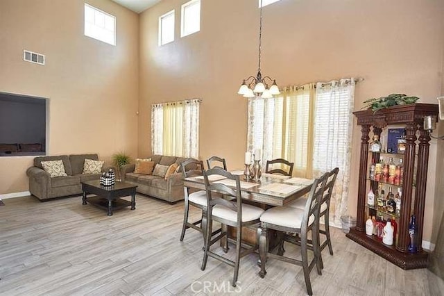 dining area featuring light hardwood / wood-style flooring, a towering ceiling, and a notable chandelier