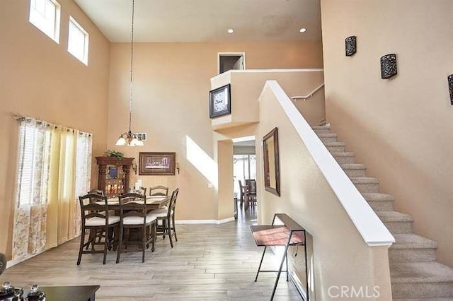 dining space featuring a notable chandelier, wood-type flooring, and a towering ceiling