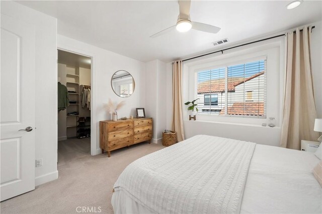 bedroom with ceiling fan, a spacious closet, light colored carpet, and a closet