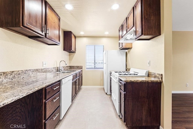 kitchen featuring light stone countertops, light wood-type flooring, dark brown cabinets, white appliances, and sink