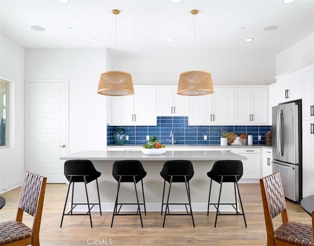 kitchen with white cabinets, hanging light fixtures, stainless steel fridge, and a kitchen island