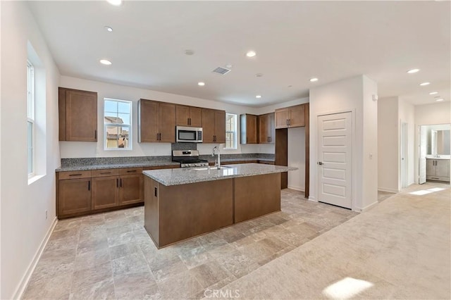 kitchen featuring light stone counters, plenty of natural light, appliances with stainless steel finishes, and an island with sink