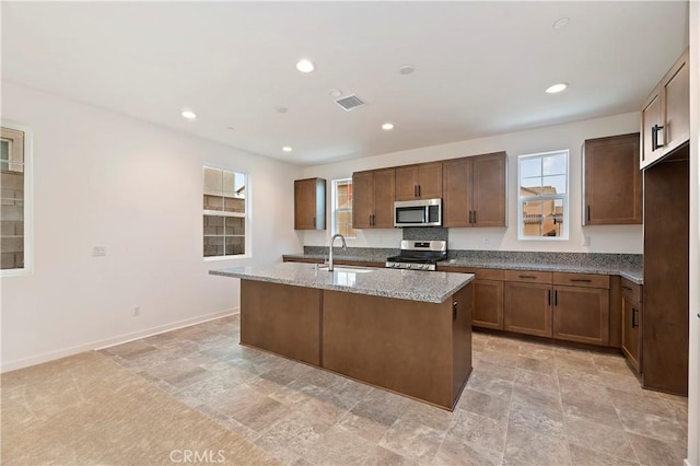 kitchen with light stone countertops, sink, stainless steel appliances, and an island with sink